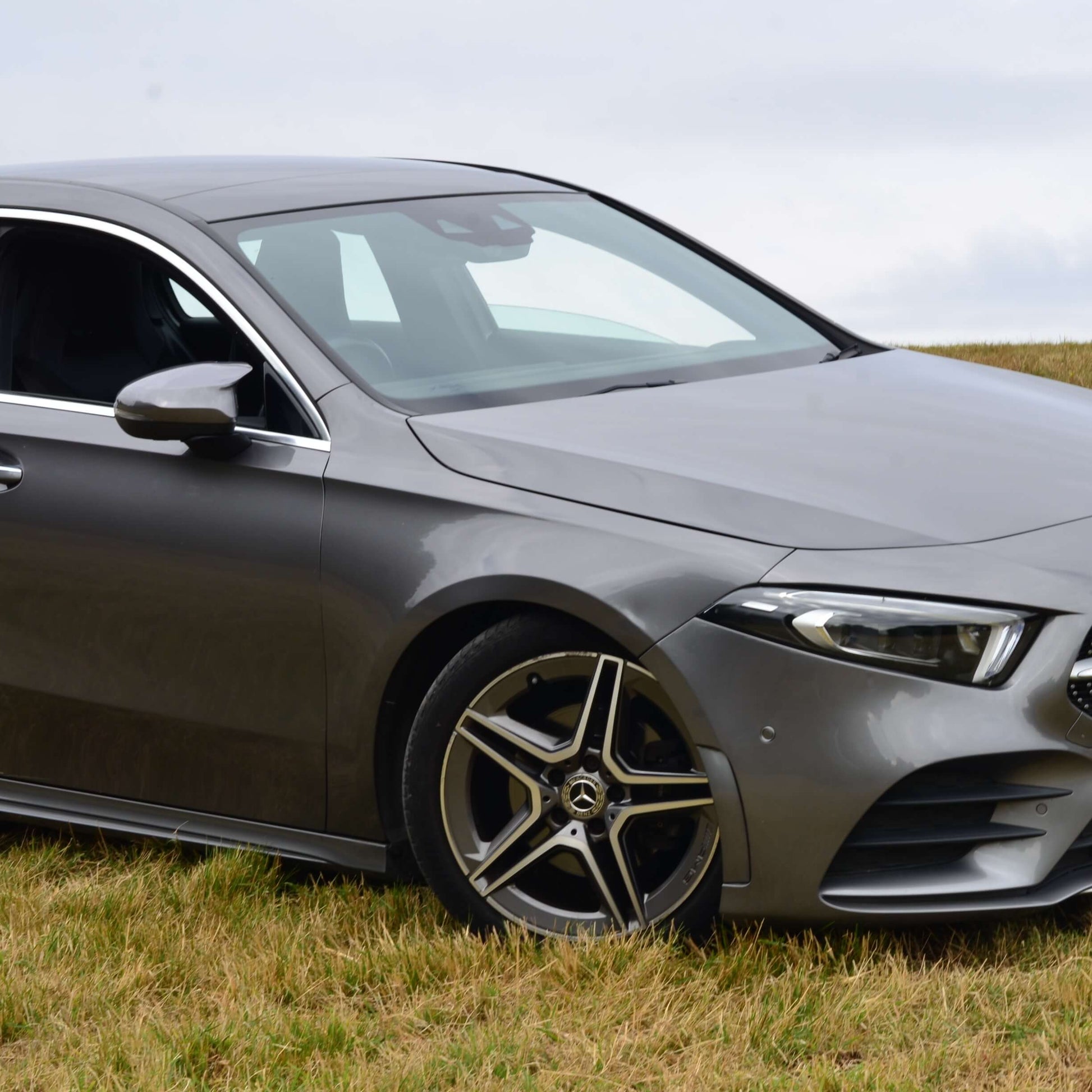 Gray Mercedes-Benz car parked on a grassy field with a cloudy sky.